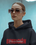 person wearing a navy bendicion unisex hoodie displayed on a light blue background with bold red bendición text across the chest and smaller white script layered over the center of the design designed by iron and velvet 62